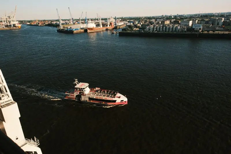 Fahrgastschiff fährt durch einen Hafen mit Kränen