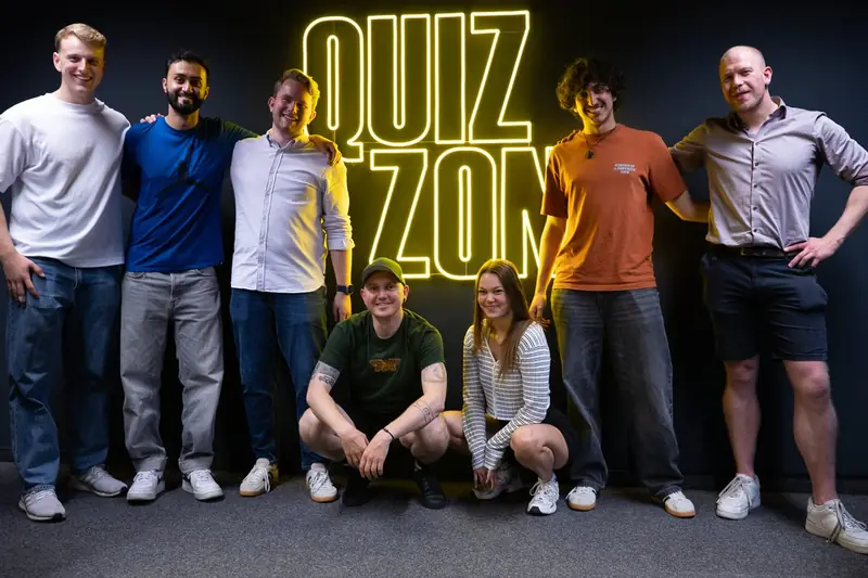 Gruppe posiert vor dem Leuchtschriftzug der QUIZ ZONE